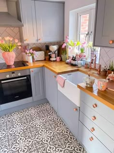 a kitchen with grey cabinets and pink flowers in vases on the counter top, next to an oven