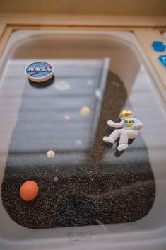 there is a small toy astronaut on the ground next to an orange ball and other items