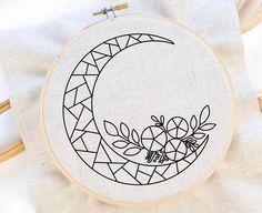 a cross stitch pattern with the moon and flowers in it on a white cloth next to a wooden hoop