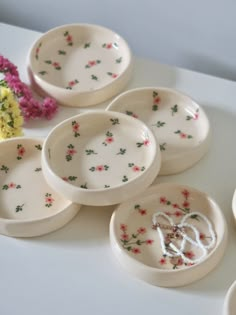 six white dishes with floral designs on them sitting on a table next to pink flowers