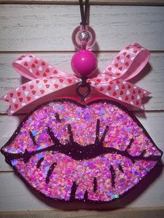 a close up of a pink and purple glitter lip on a wooden surface with a ball hanging from the hook