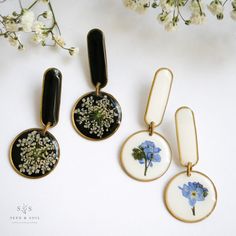 three pieces of jewelry sitting next to each other on a white surface with flowers in them