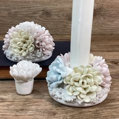 two white vases with pink and blue flowers on them next to a lit candle