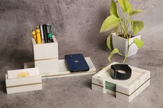 an assortment of office supplies sitting on a table next to a potted plant and cell phone