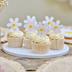 cupcakes with white frosting and yellow centers on a plate next to flowers