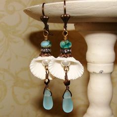 a pair of blue and white earrings hanging from a hook on a stand next to a wall