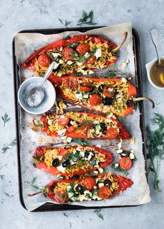 stuffed red peppers on a baking sheet with olives, tomatoes and other toppings