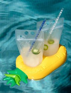 two plastic cups filled with drinks floating on top of a yellow raft in the water