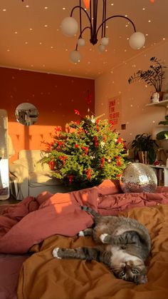 a cat laying on top of a bed next to a christmas tree in a room