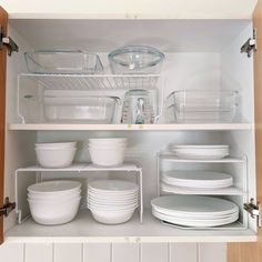 an open cabinet filled with white dishes and glasses on top of each other in a kitchen