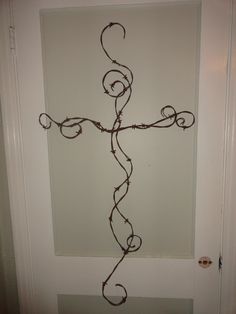 a cross made out of barbed wire hanging from the side of a door with a white wall behind it