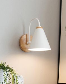 a white lamp mounted on the wall next to a potted plant