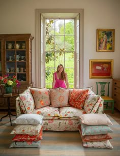 a woman sitting on top of a floral couch in front of a large open window