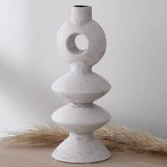 a white vase sitting on top of a wooden table next to dry grass and a wall