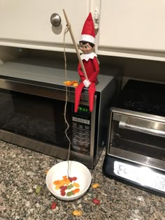 an elf is sitting on top of a toaster oven with gummy bears in front of it