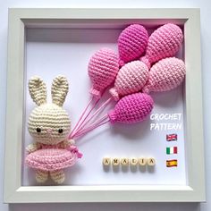 a crocheted bunny holding balloons in a frame with the word love spelled below it