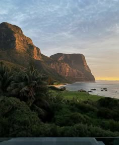 the mountains are next to the ocean with palm trees in front of them and an empty swimming pool