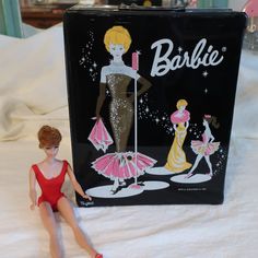 a barbie doll sitting on top of a bed next to a black bag that says barbie