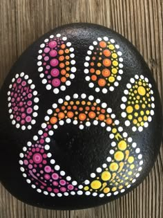 a painted rock with an animal's paw print and dots on the rocks is sitting on a wooden surface