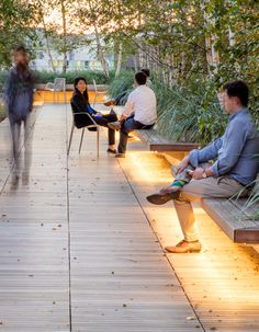 people sitting on benches in the park at night with lights coming from them and trees lining the walkway