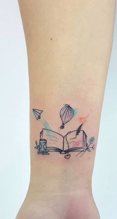 an open book tattoo on the ankle with hot air balloons flying over it and books