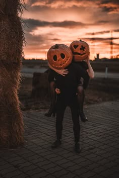 two people are hugging each other with pumpkins on their heads in front of a sunset