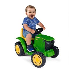 a little boy riding on the back of a green toy tractor with yellow tires and smiling