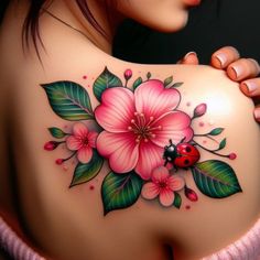 a ladybug and flower tattoo on the back of a woman's shoulder