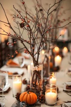 a centerpiece with candles, branches and pumpkins sits on a dining room table