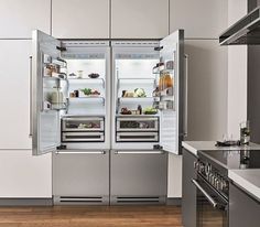 an open refrigerator in a kitchen with wooden floors and white walls, along with stainless steel appliances