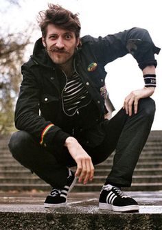 a man is squatting down on the steps with his hands in his pockets and wearing black sneakers