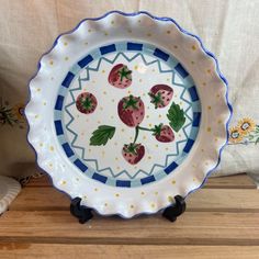 a blue and white plate with strawberries painted on the side sitting on a wooden table