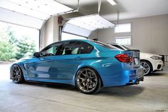 two cars are parked in a garage with their doors open and one is shiny blue