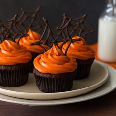 chocolate cupcakes topped with orange frosting and spider web decorations on a plate