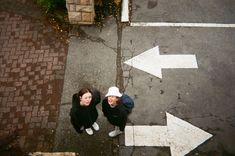 two people standing next to each other near an arrow pointing in opposite directions on the street