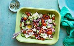 a green bowl filled with cucumbers, tomatoes and other veggies next to a spoon