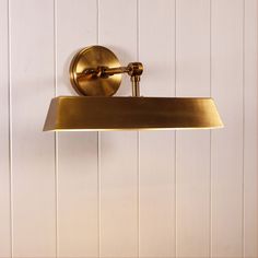 a brass bathroom light mounted on a white wall with wood planks in the background