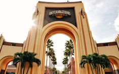 the entrance to an amusement park with palm trees in front and sun shining on it