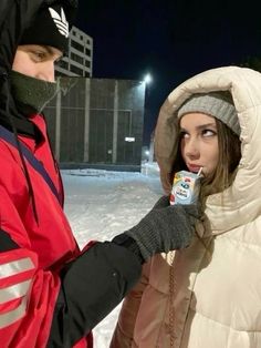 two people standing in the snow one is wearing a winter coat and the other has a cold drink