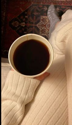 a person holding a cup of coffee in their hand on top of a bed with a rug