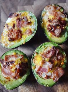 four avocado halves with bacon and cheese on them sitting on a wooden surface