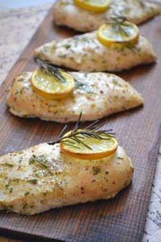 three pieces of chicken with lemons and rosemary on them sitting on a cutting board