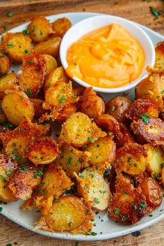 a white plate topped with fried potatoes covered in cheese and sauce next to a bowl of dip