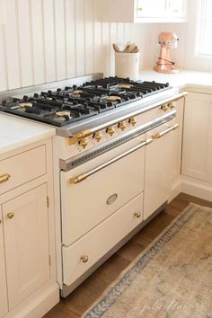 a stove top oven sitting inside of a kitchen next to white cupboards and drawers