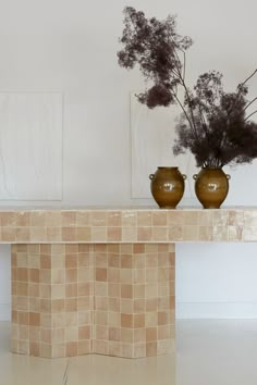 two vases with flowers on a table in front of a white wall and paintings