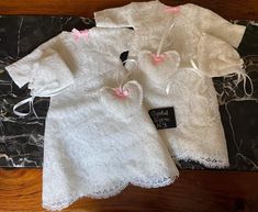 two white baby clothes with pink bows on them sitting on a marble slab topper