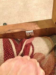 a person is holding something in their hand while sitting on the floor next to a piece of furniture