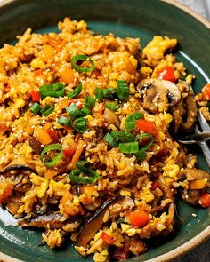 a green plate topped with rice and vegetables next to a fork on top of a table