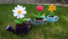 three crocheted watering can with flowers in them sitting on the grass next to a fence