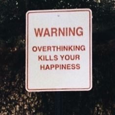 a warning sign posted on a pole in front of some bushes and trees with the words,'warning overthiking kills your happiness '